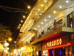 A multi-story building with a prominent 'El Paradiso' sign, balconies, and a busy street scene at night. - Greta Apartments (Hersonissos)