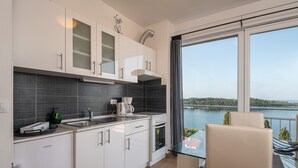 A modern kitchen with white cabinets, a black backsplash, and a view of a lake through large windows. - Apartments Didan (Konavle)