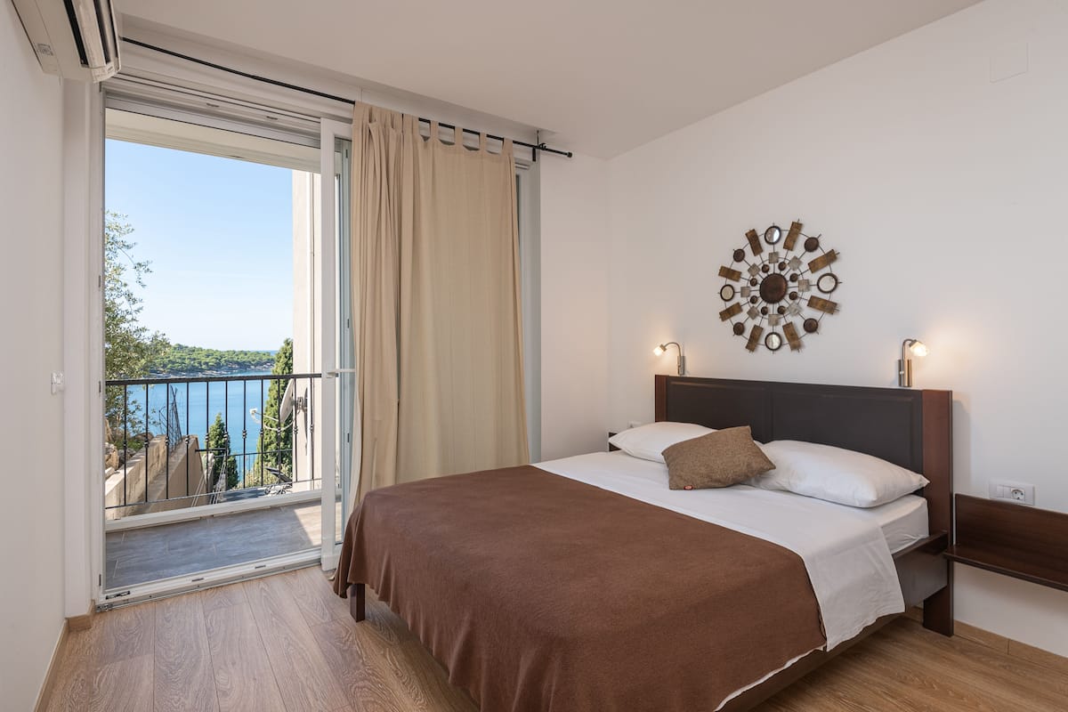 A bedroom with a large bed, a view of the sea, and a balcony with a railing.
