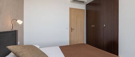 Hotellihuone, jossa on sänky, yöpöytä, lamppu, vaatekaappi ja ilmastointilaite.