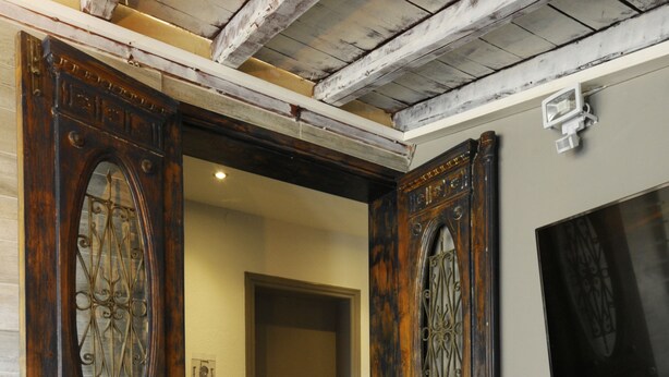 A hallway with ornate wooden doors, a tiled floor, and a wall-mounted television. - Skianthion (Skiathos)