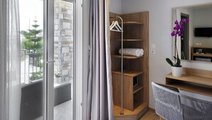 A modern hotel room with a stone wall, a wooden shelf unit, a mirror, and a view of the outside balcony. - Skianthion (Skiathos)