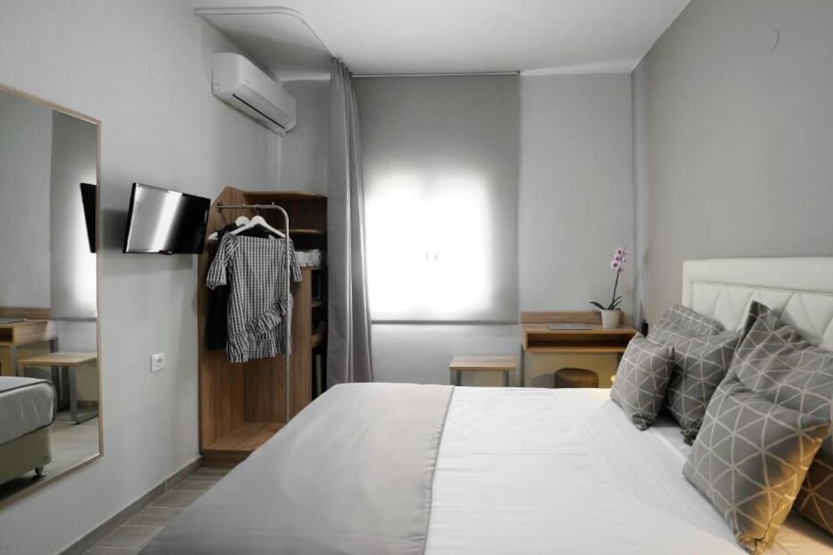 Un dormitorio moderno con una cama grande, un televisor en la pared, un armario y una mesita de noche pequeña con una lámpara.