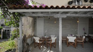 An outdoor patio with a pergola, wooden chairs, a table, and hanging lights. - Skianthion (Skiathos)