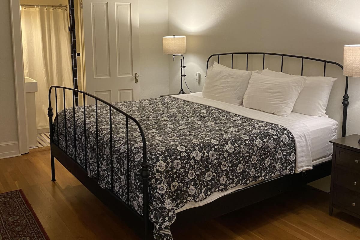 Une chambre à coucher avec un lit, une table de chevet, une lampe, un ventilateur de plafond et une porte.