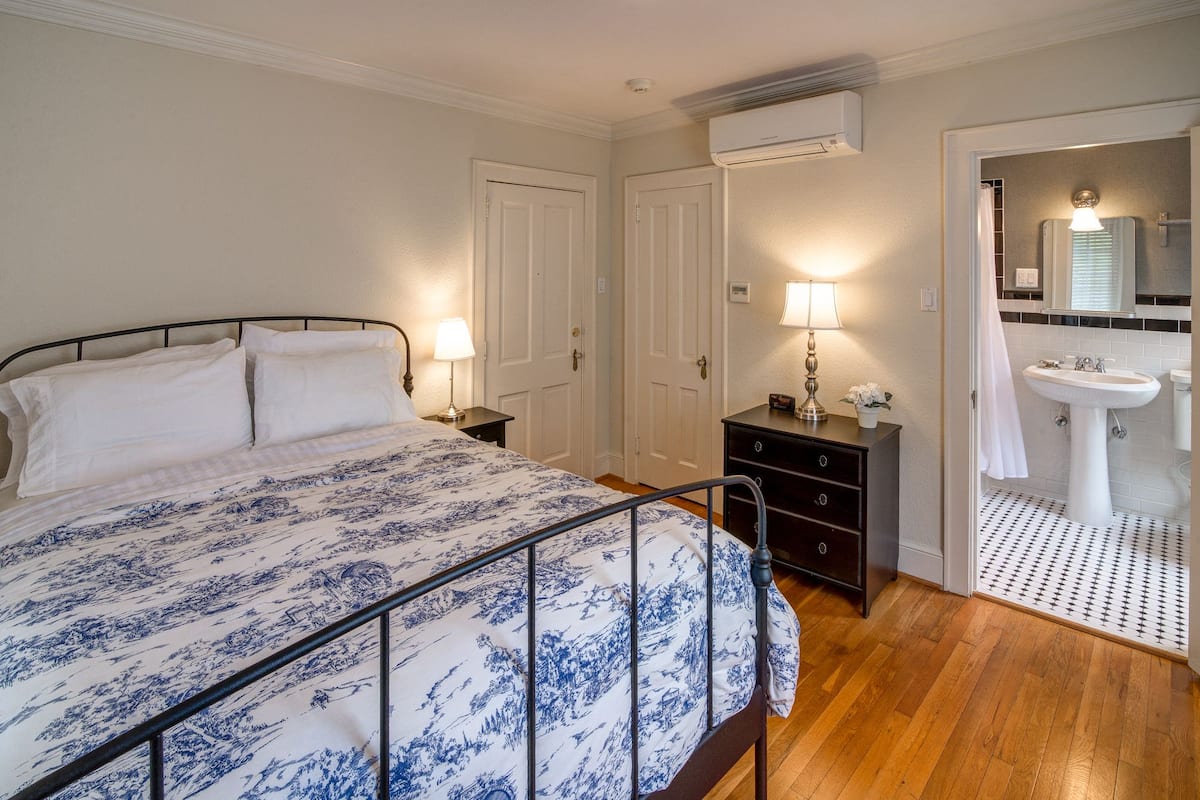 Une chambre à coucher comprenant un lit, des lampes de chevet, une commode, un miroir et une salle de bain avec un lavabo et une douche.