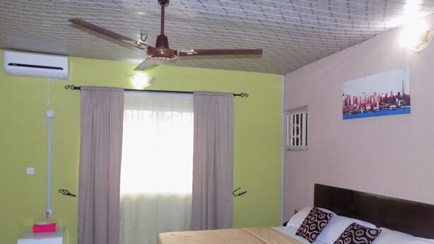 A bedroom with a bed, curtains, a ceiling fan, a window, and a wall-mounted air conditioner. - Posh Apartments (Lagos)