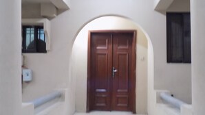 A hallway with a double wooden door, white walls, and a small window on the left. - Posh Apartments (Lagos)