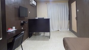 A hotel room with a bed, a desk, a chair, a television, and a curtain. - Posh Apartments (Lagos)