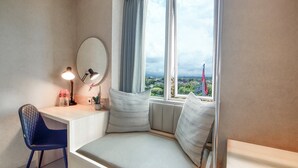 Una habitación con escritorio, silla y asiento junto a la ventana con vistas a la ciudad.
