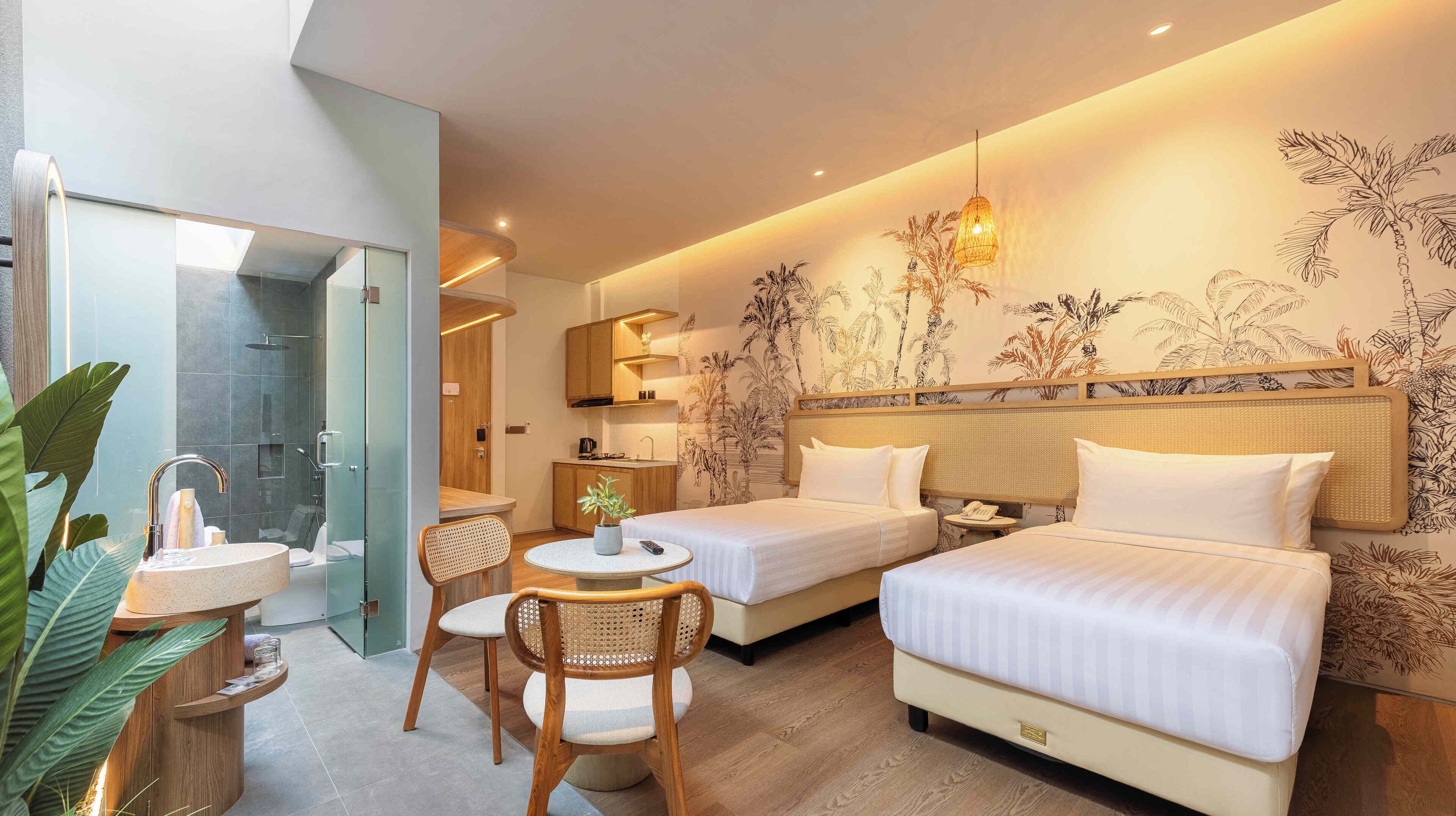 Ein Hotelzimmer mit zwei Betten, einer kleinen Essecke, einem Badezimmer mit Duschkabine und einer Küchenzeile.