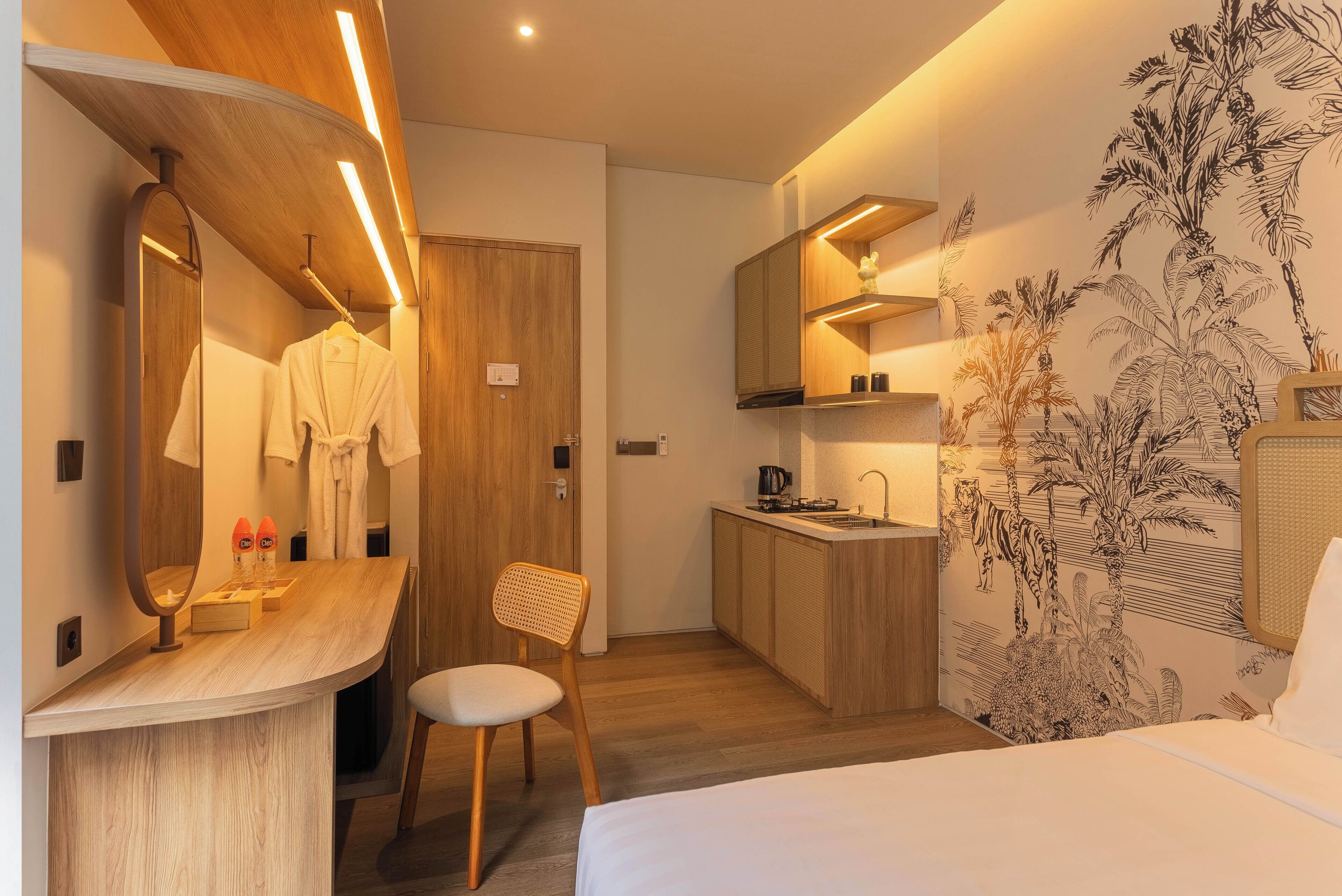 Quarto de hotel moderno com toucador de madeira, cama, pequeno kitchenette e casa de banho.