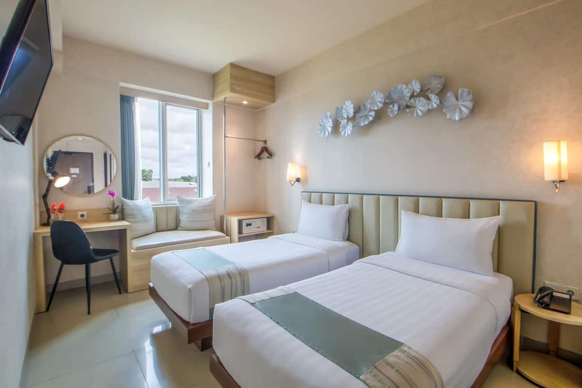 Hotelkamer met twee bedden, een bureau, een stoel, een televisie, een spiegel en decoratieve wandkunst.