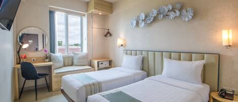 A hotel room with two beds, a desk, a chair, a TV, a mirror, and decorative wall art.