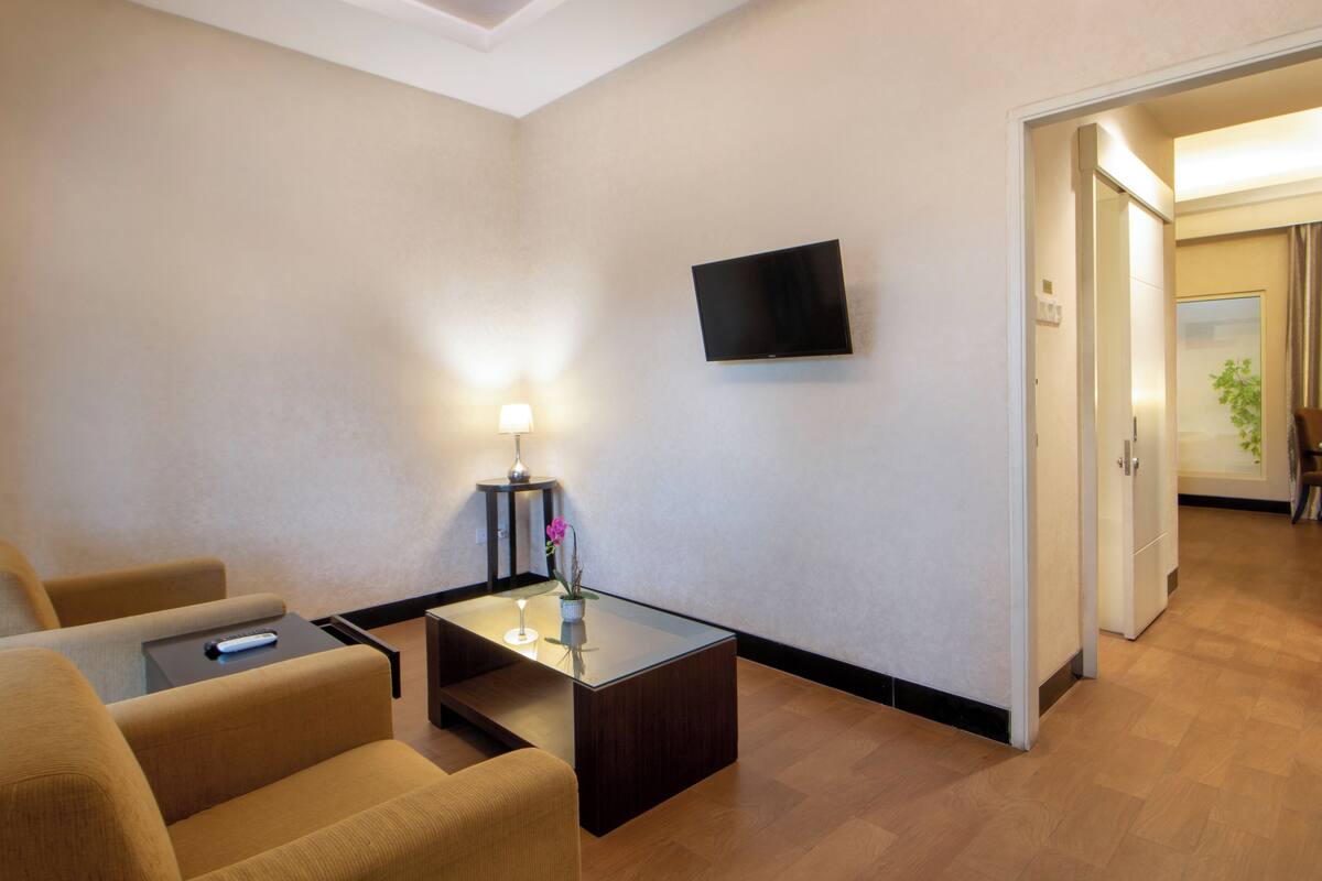 Een hotelkamer met een bank, een bijzettafeltje, een flatscreen televisie aan de muur en een lamp op een nachtkastje.
