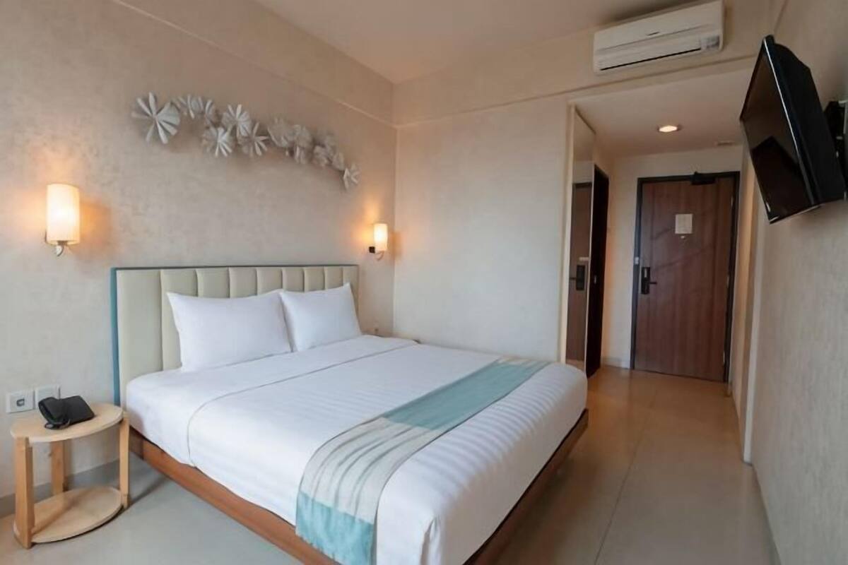 Een hotelkamer met een bed, nachtlampjes, een flatscreen-tv en een airconditioning.