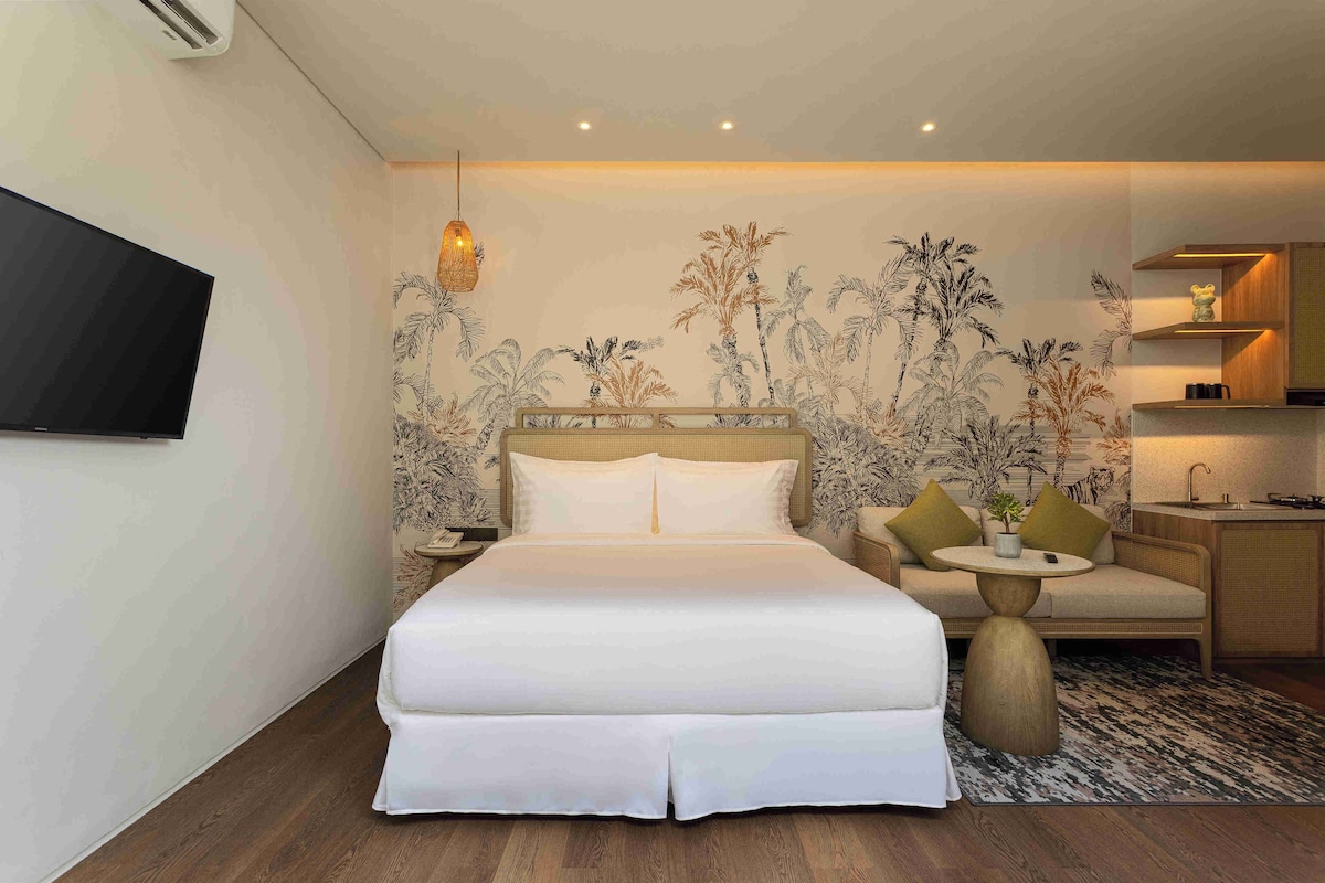 Una habitación de hotel con cama, televisión, una mesita, sofá y una zona de cocina.