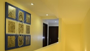 A hallway with a series of framed artworks on the wall, a staircase leading to an upper floor, and a door at the end of the hallway.