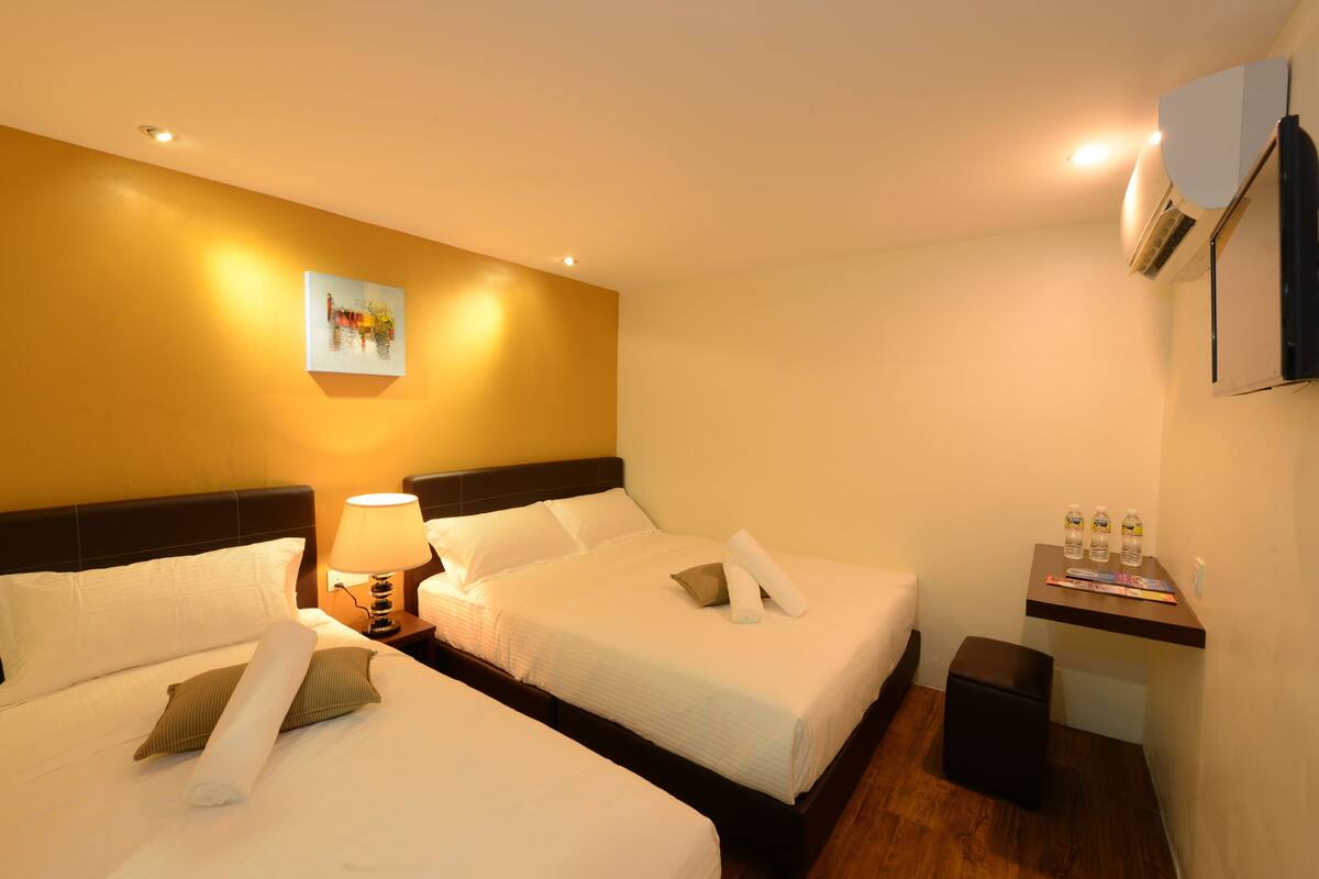 Ein Hotelzimmer mit zwei Betten, einem Nachttisch mit Lampe, einem kleinen Schreibtisch mit Stuhl und einer Klimaanlage an der Wand.