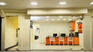 A modern kitchen with a glass partition, a reception area with orange furniture, and a staircase leading to another floor.