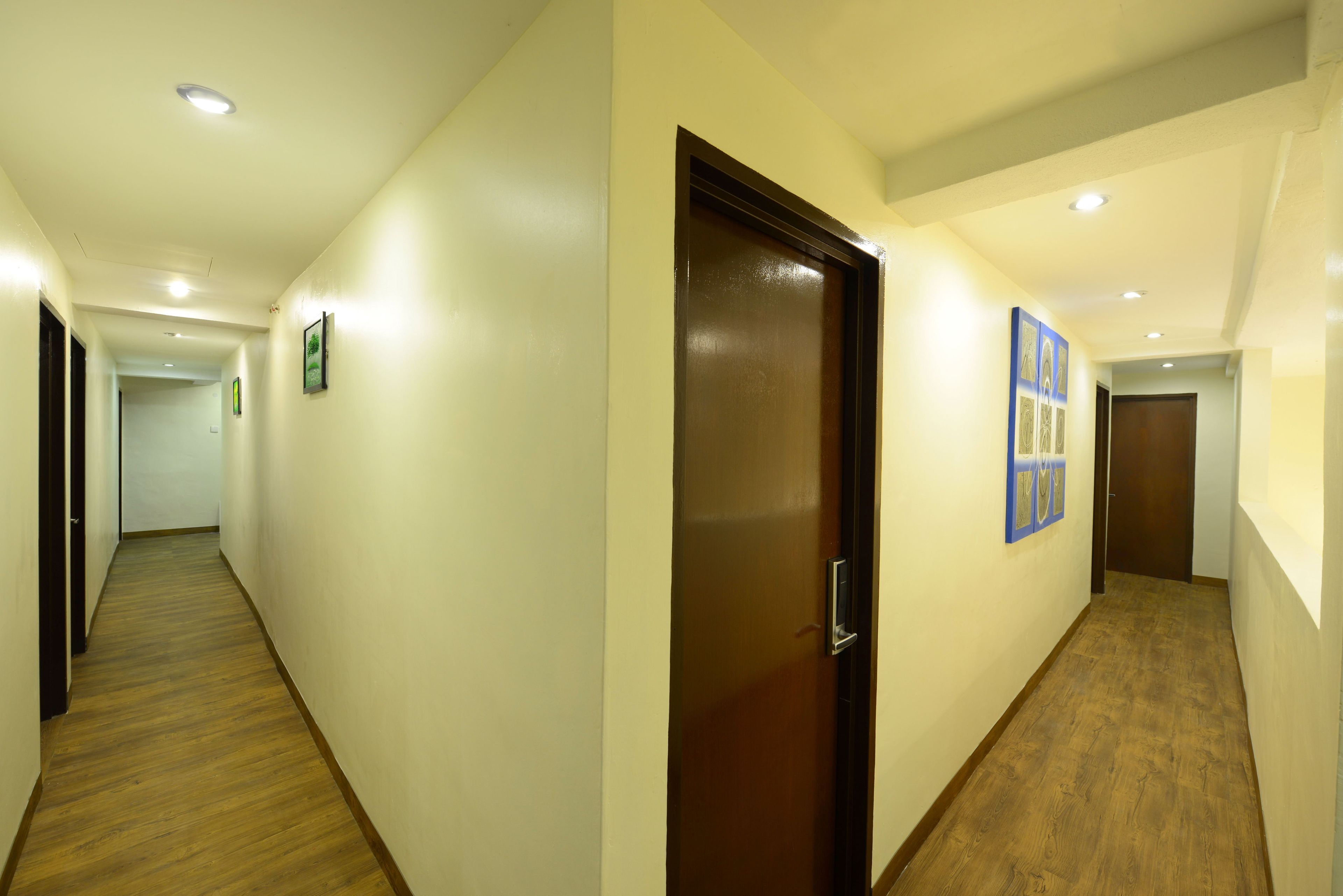 Un couloir avec un plancher en bois, une porte marron et des tableaux encadrés accrochés aux murs.