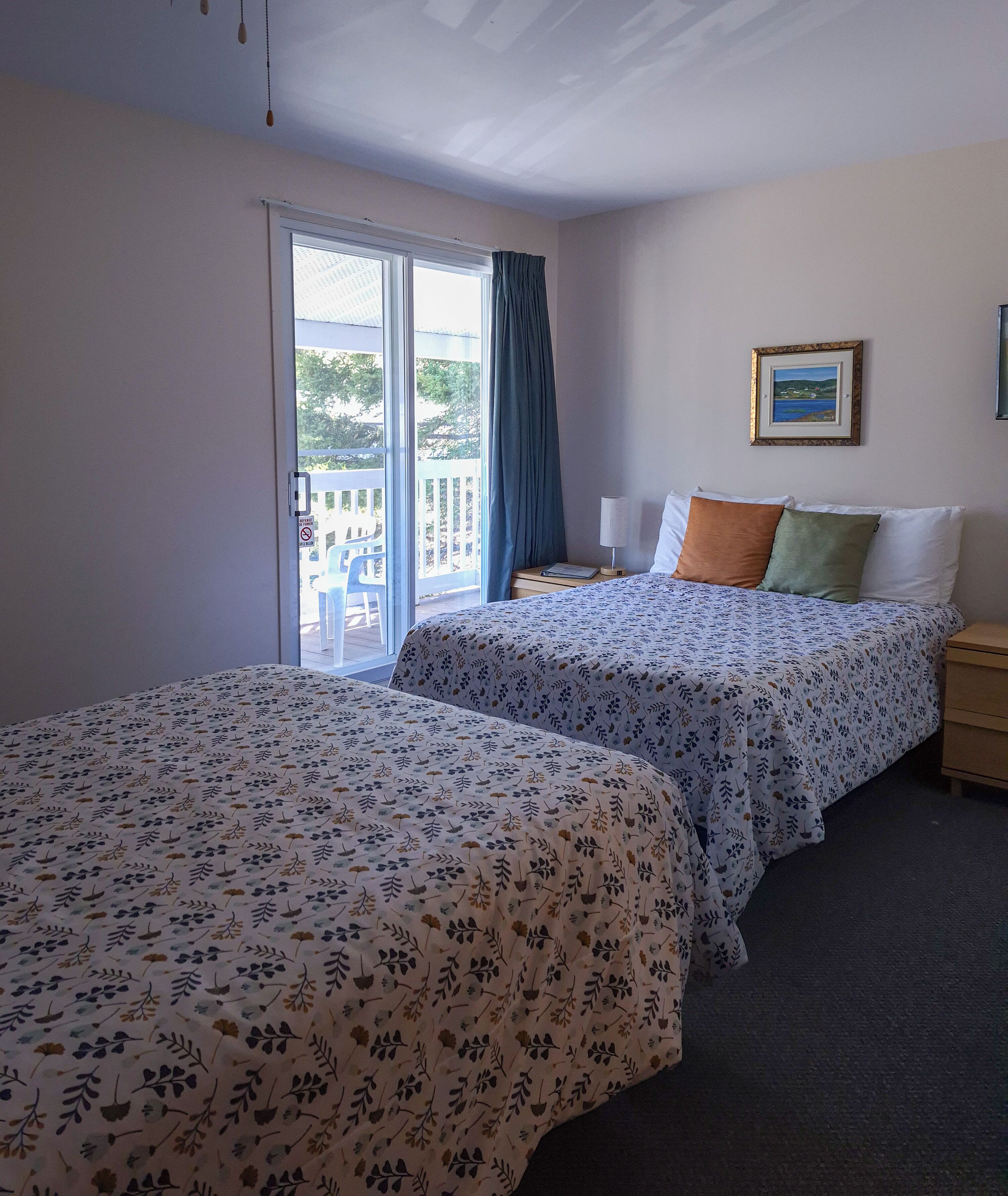 Habitación de hotel con dos camas, un ventanal con vistas, un cuadro en la pared y una mesita de noche.