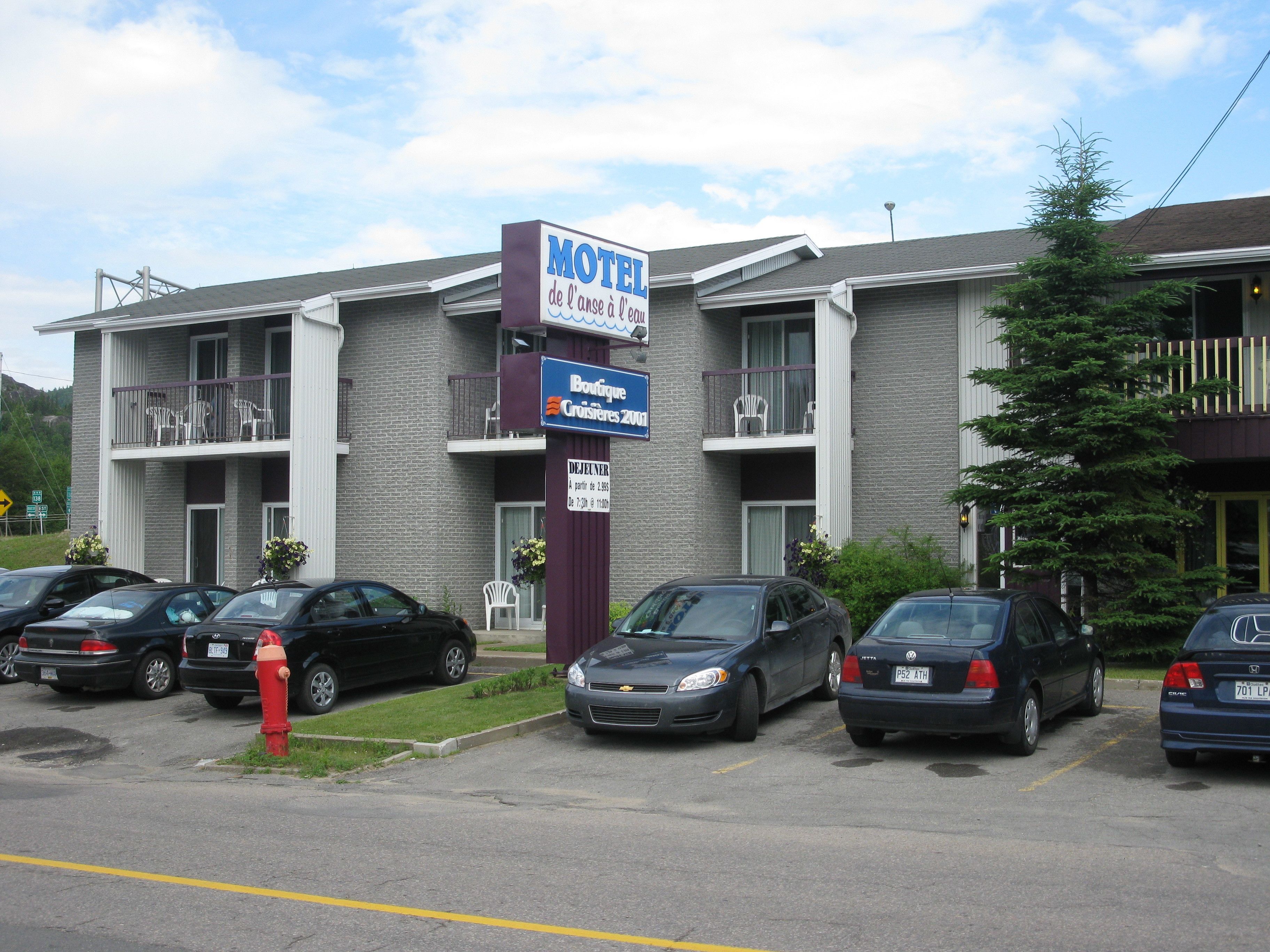 A motel with a signboard, a parking lot with several cars, and a building with balconies.