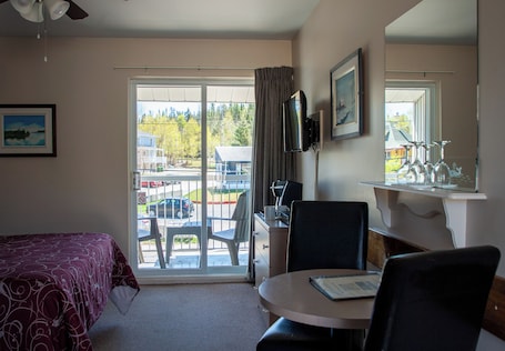 A hotel room with a bed, a desk with a chair, a television, and a window with a view of the outside.. Motel de l'Anse à l'Eau