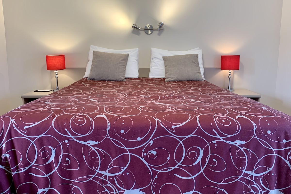 Una cama bien hecha con una colcha estampada, dos almohadas y dos lámparas de noche.