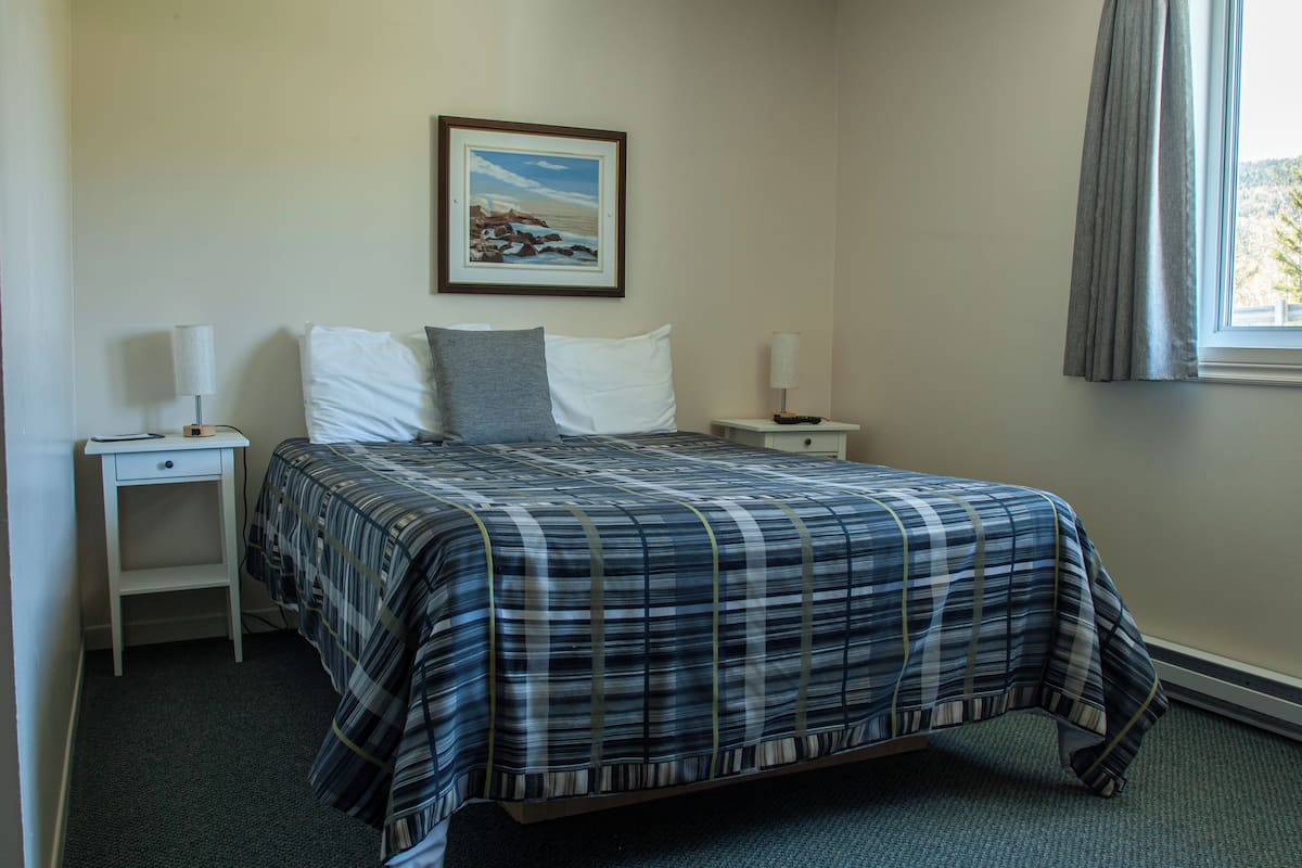 Un dormitorio con una cama, dos mesitas de noche, un cuadro en la pared y una ventana con cortinas.