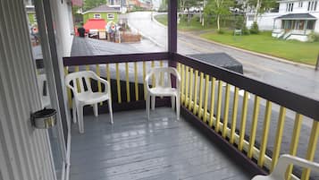 A covered porch with two white plastic chairs, a metal pot, and a yellow railing.