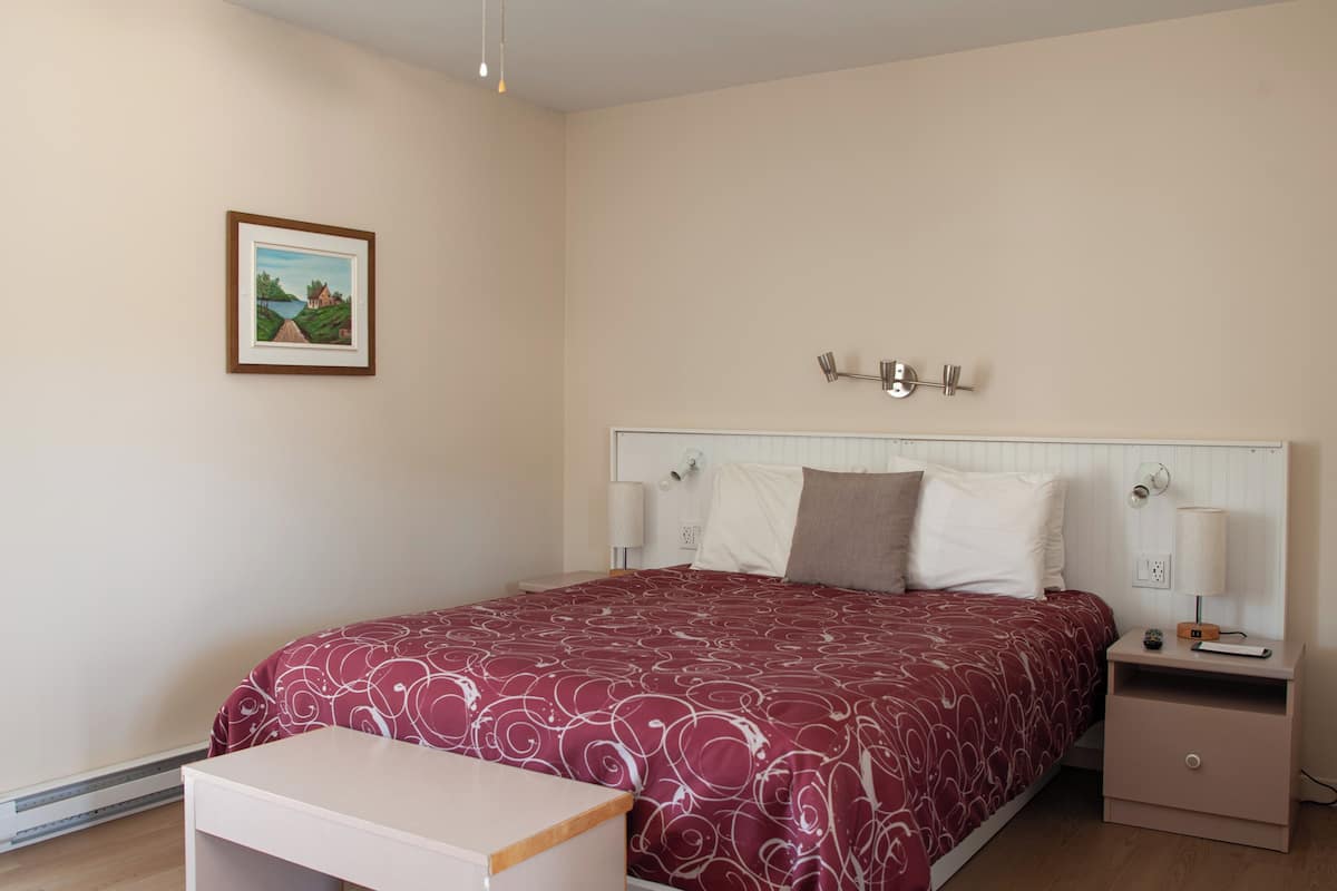 Un dormitorio con cama, mesitas de noche, lámpara, un cuadro en la pared y un banco.