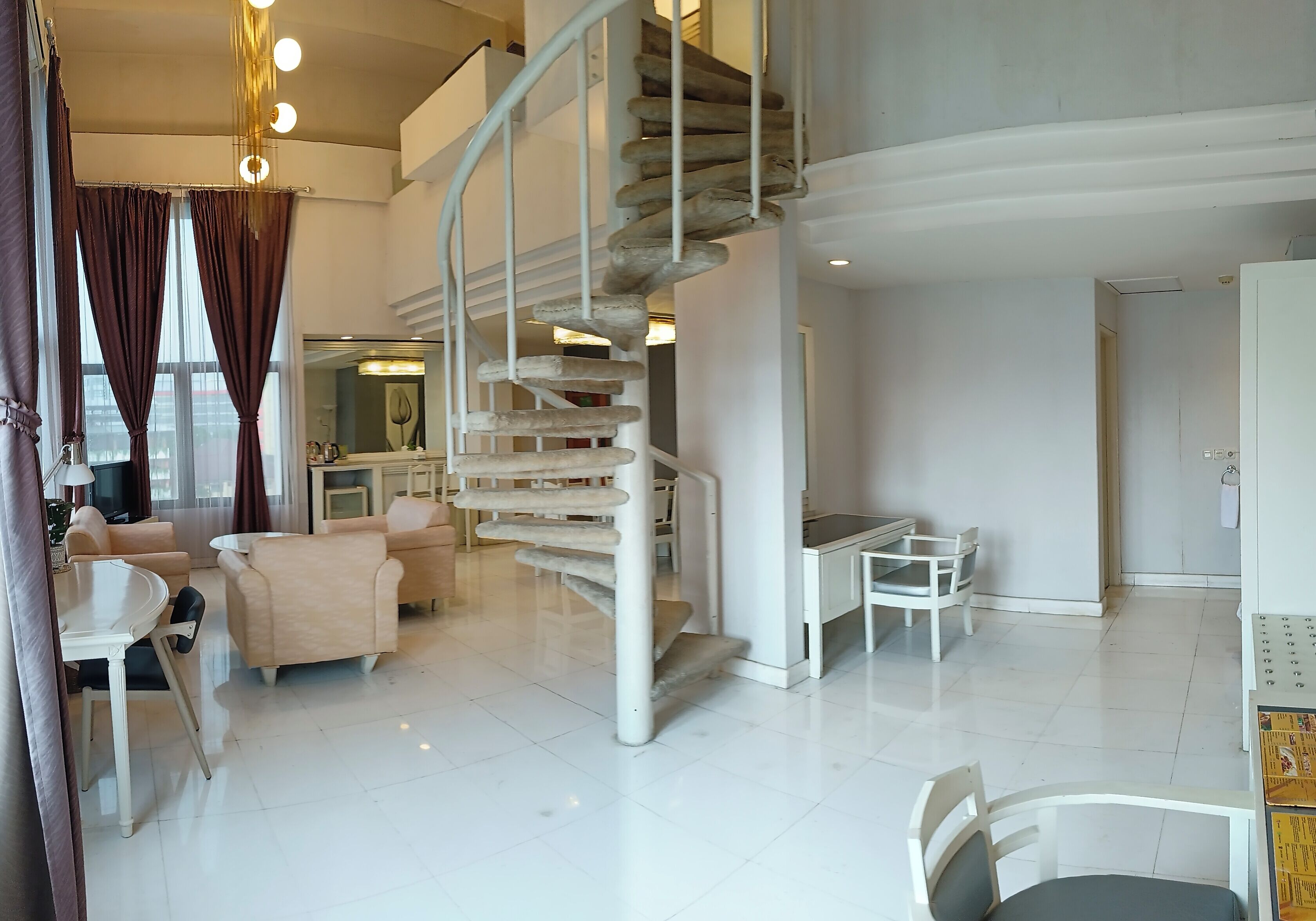 A modern living area with a spiral staircase, a dining table, sofas, and a kitchen area.