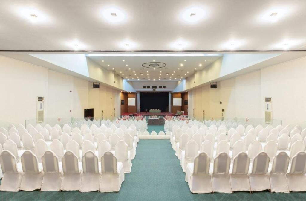 A large conference room with rows of white chairs, a stage at the front, and a green carpet.