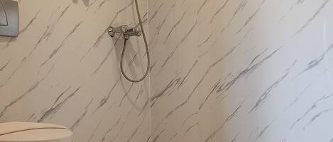 Un baño con pared de mármol, inodoro y ducha con cabezal de ducha manual.