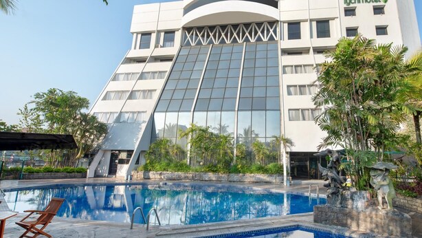 A modern hotel with a large glass facade, a swimming pool, and tropical landscaping. - Tychi Hotel (Malang)