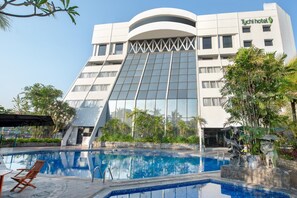 A modern hotel with a large glass facade, a swimming pool, and tropical landscaping. - Tychi Hotel (Malang)