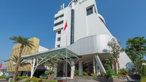 A modern hotel with a unique architectural design, featuring a prominent flag and a covered entrance area. - Tychi Hotel (Malang)
