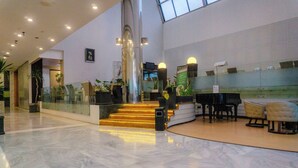 A spacious lobby with a marble floor, a grand staircase, and a seating area with a piano. - Tychi Hotel (Malang)
