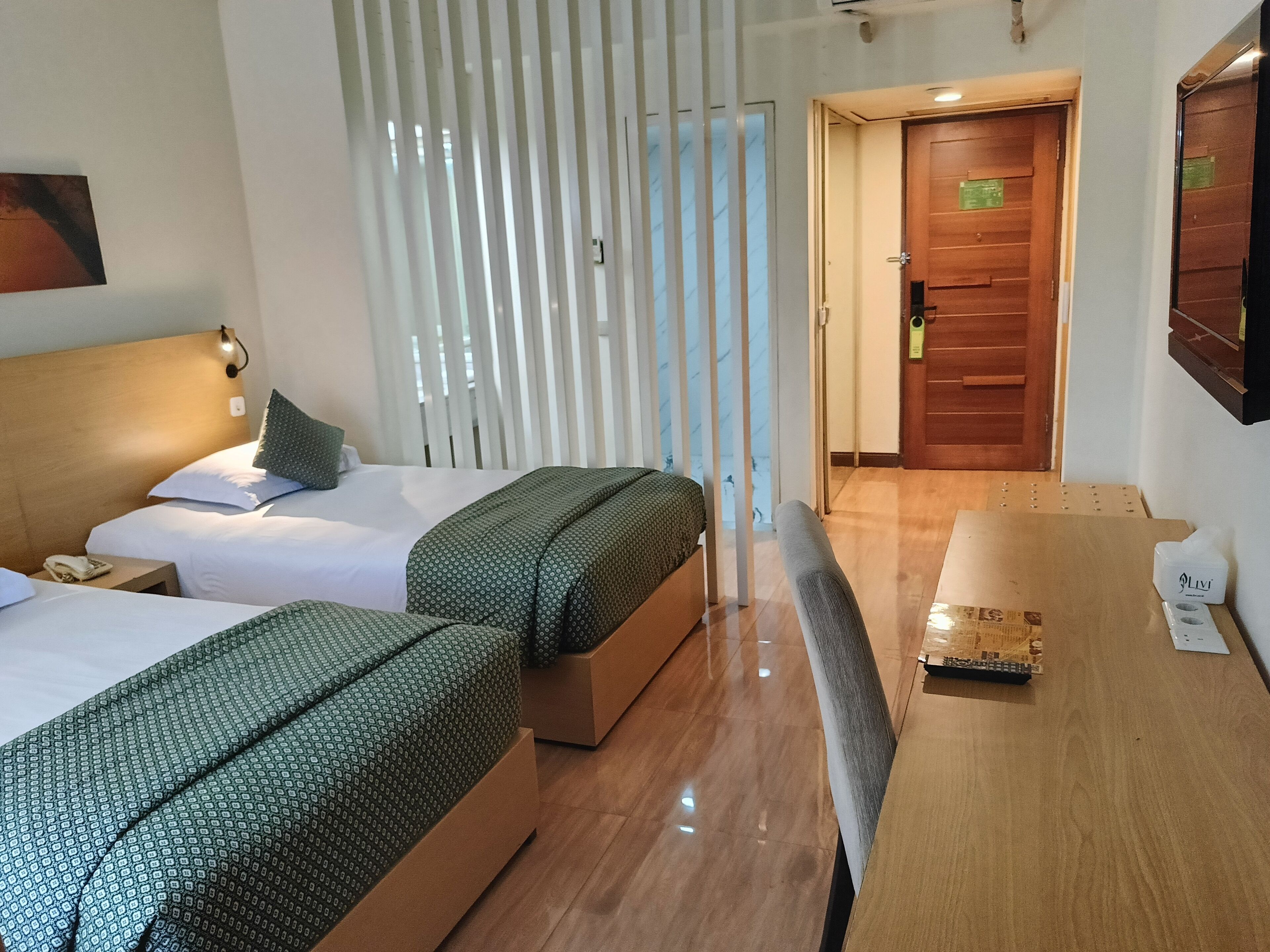 A hotel room with two beds, a wooden desk, a telephone, and a door leading to another room.