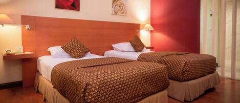 A hotel room with two beds, each with patterned bedding and pillows, a wooden headboard, and wall-mounted lamps.