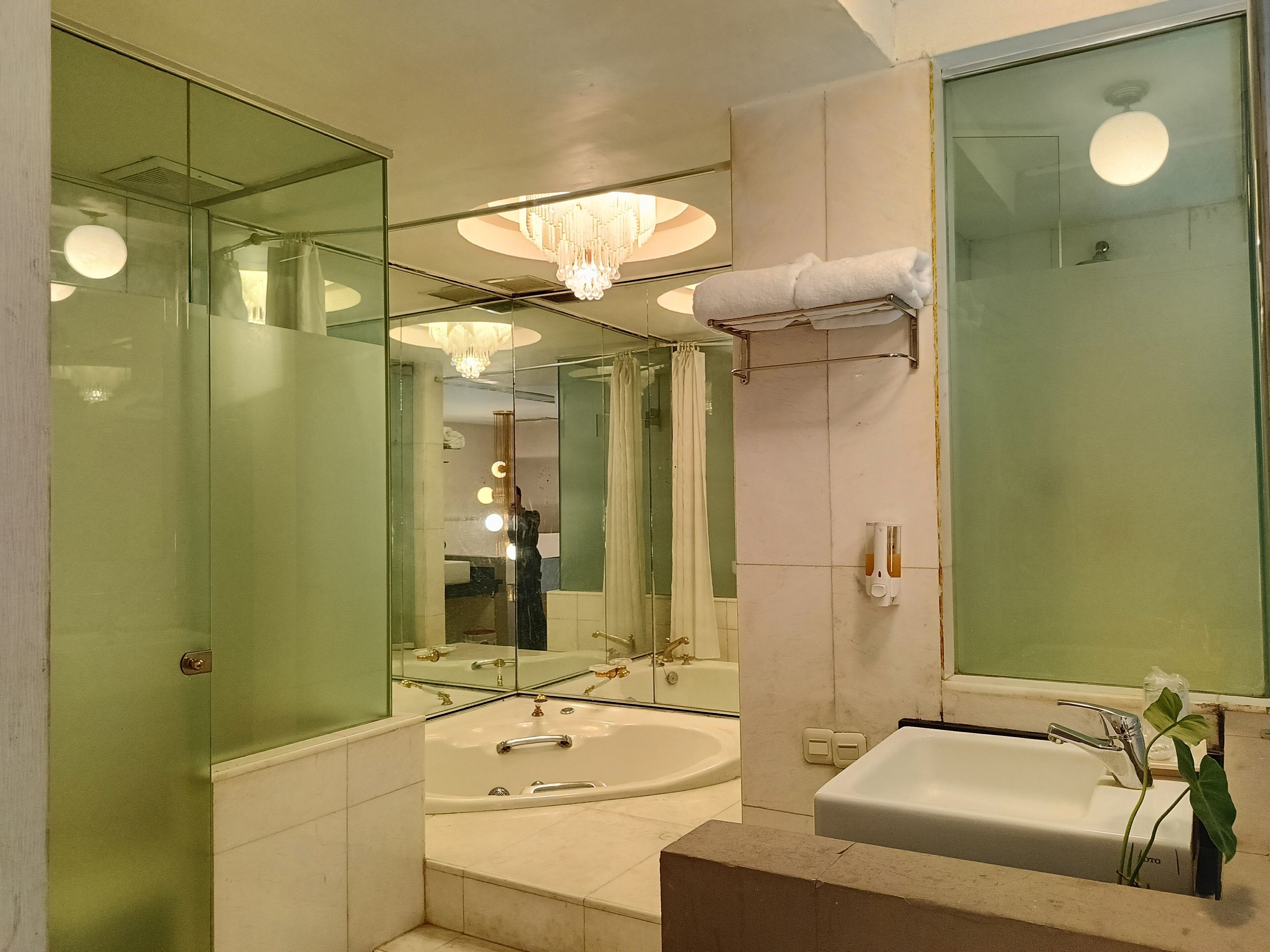 A modern bathroom with a large mirror, a chandelier, a bathtub, and a sink.