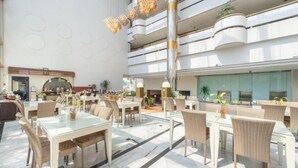 A spacious indoor dining area with multiple tables and chairs, a high ceiling with decorative lighting, and a modern architectural design. - Tychi Hotel (Malang)