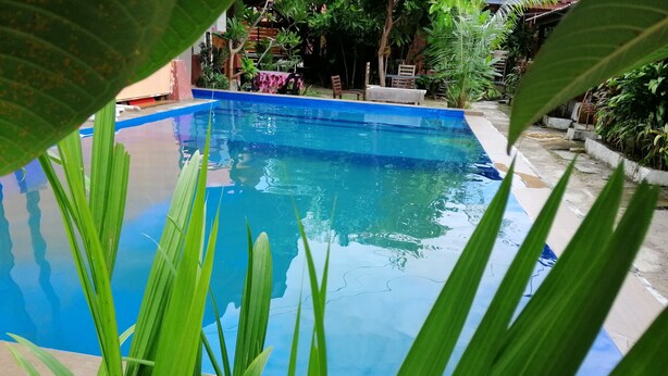 A clear view of a swimming pool surrounded by greenery and a patio area with outdoor furniture. - The Village Langkawi (Langkawi)