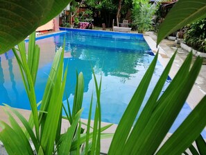 A clear view of a swimming pool surrounded by greenery and a patio area with outdoor furniture. - The Village Langkawi (Langkawi)