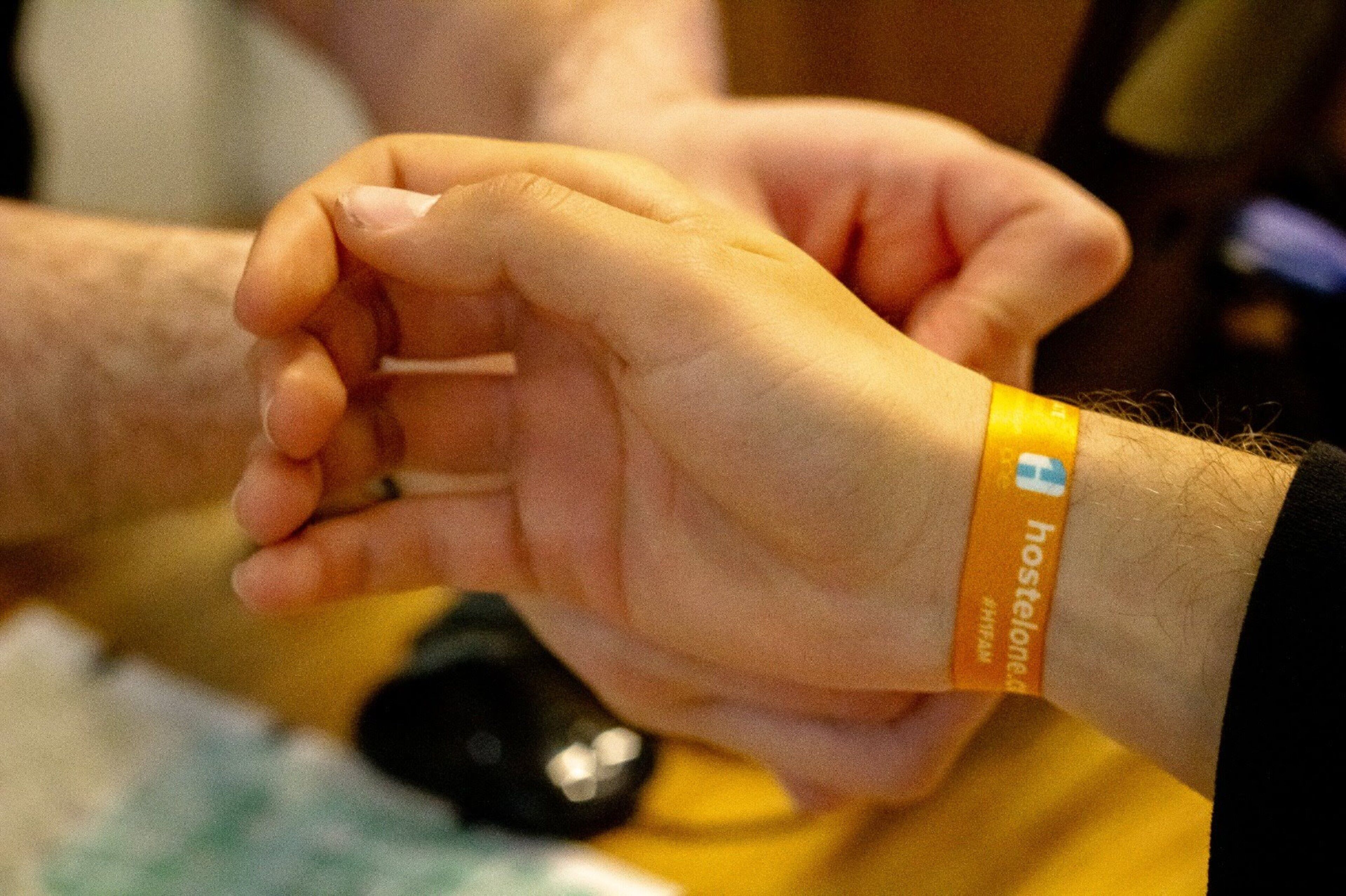 Manos sosteniendo un objeto pequeño, con una pulsera que dice 'hostelone.de'.