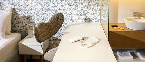 Une chambre d’hôtel moderne avec un lit blanc, une table de chevet avec une lampe, une chaise et une petite table sur laquelle se trouvent un sac à main et une brosse.