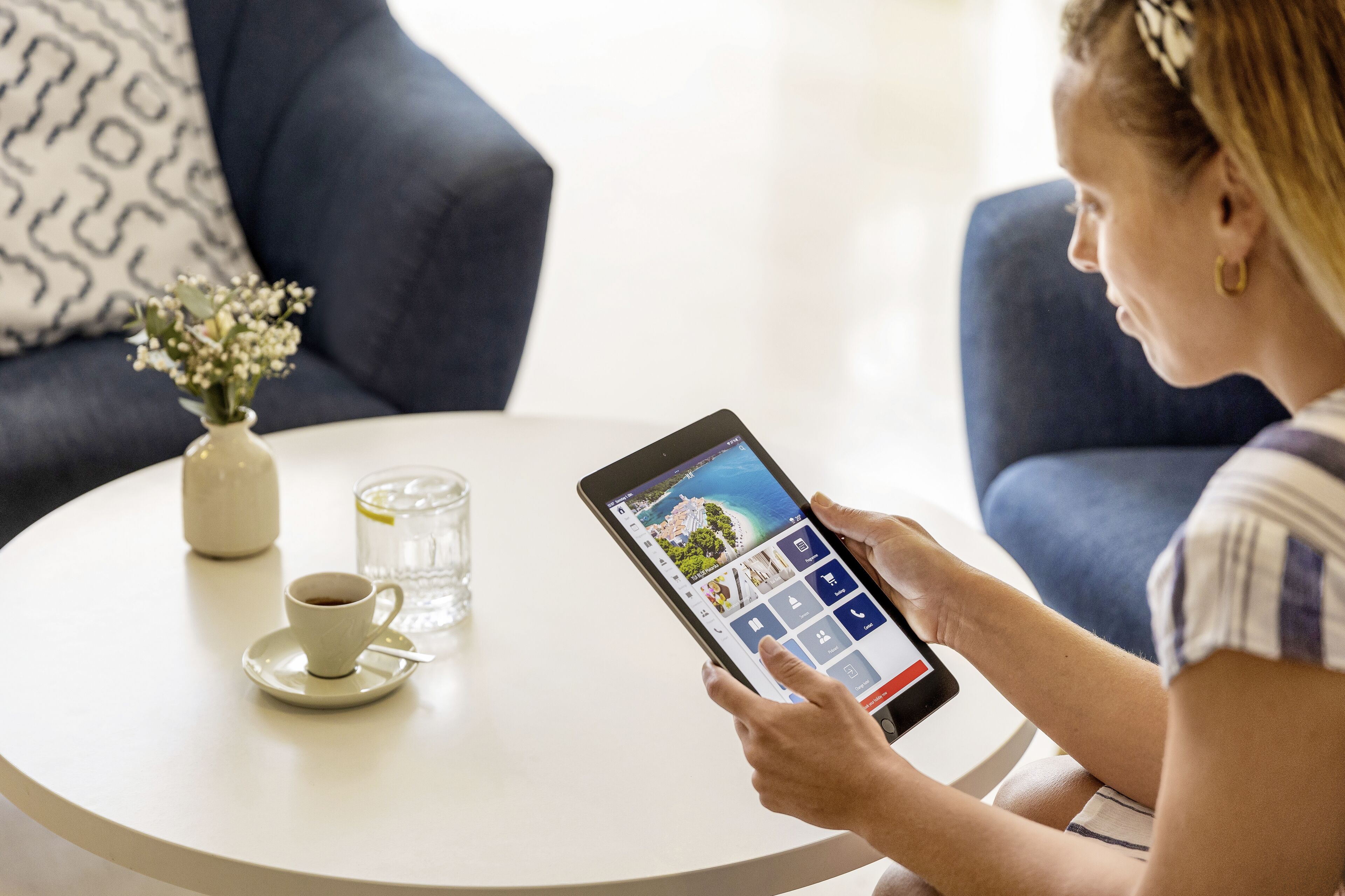 A person using a tablet on a round white table with a cup and a glass of water.