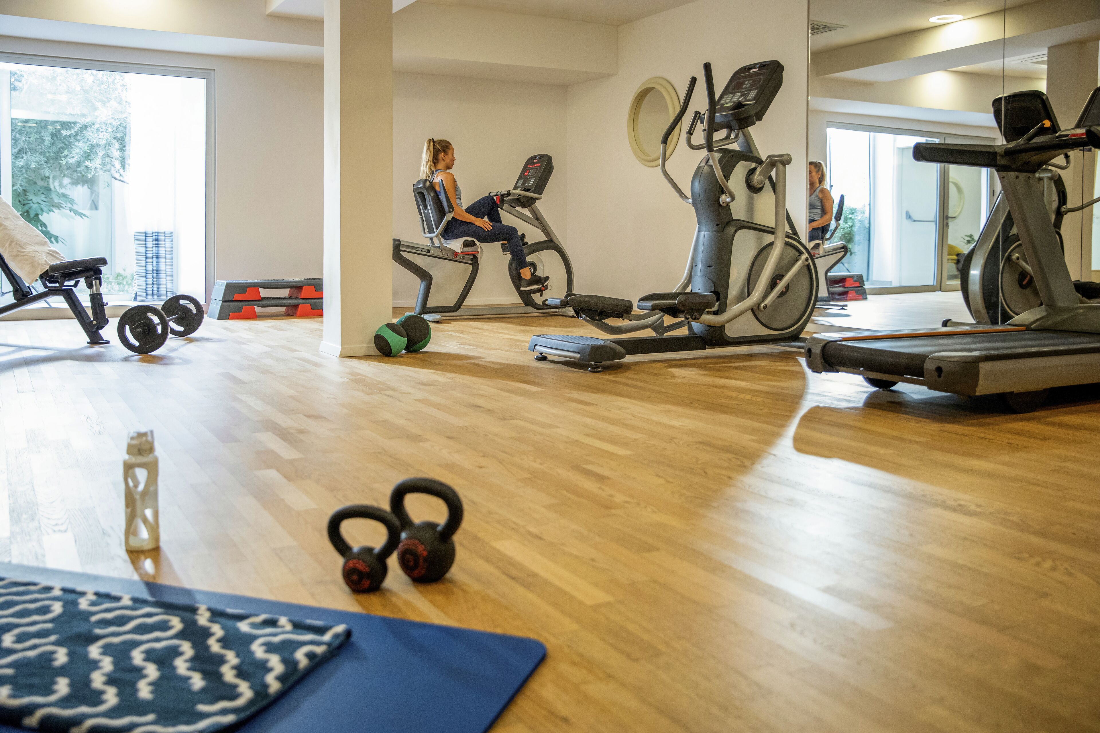 A gym with exercise equipment, a large mirror, and a wooden floor.
