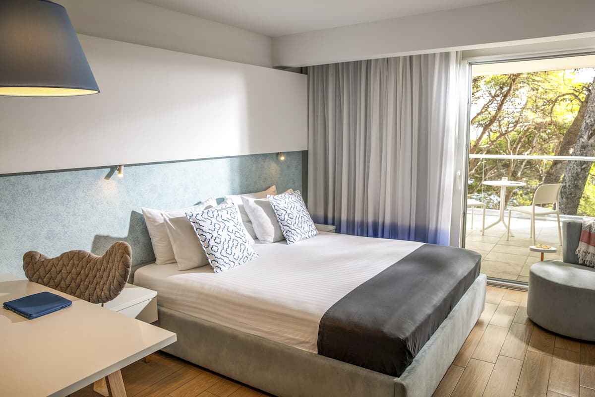 A modern hotel room with a large bed, a desk, and a view of the outdoors.